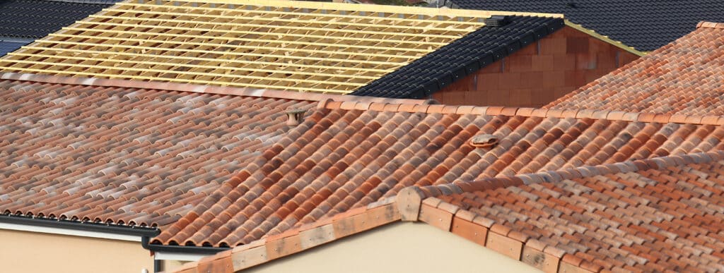 Toits avec tuiles terre cuite, construction toit neuf avec lattes bois, tuiles noires et panneaux solaires. Vue aérienne.
